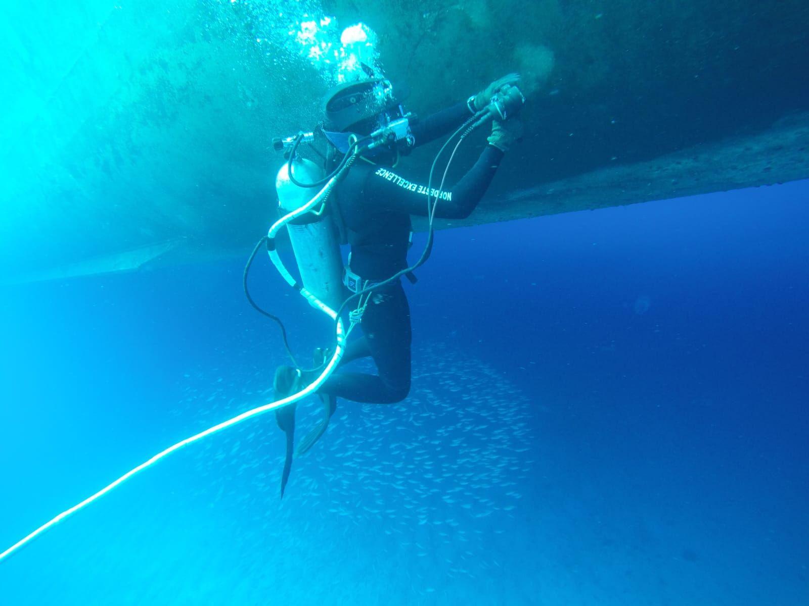 Underwater diver using equipment to clean the hull of a boat, surrounded by clear blue water submarino, manutenção, inspeção