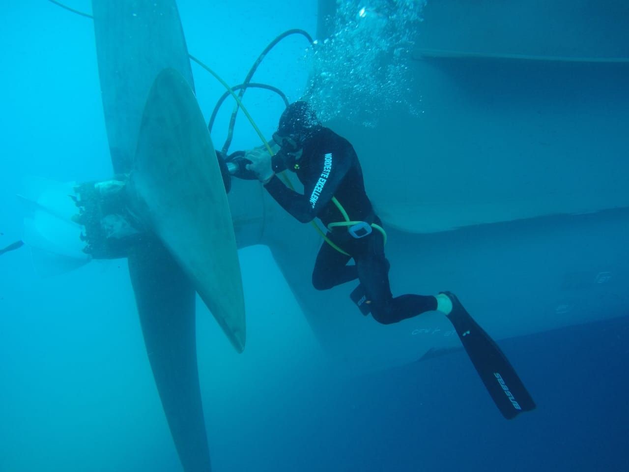 Diver inspecting large ship propeller underwater with bubbles surrounding.