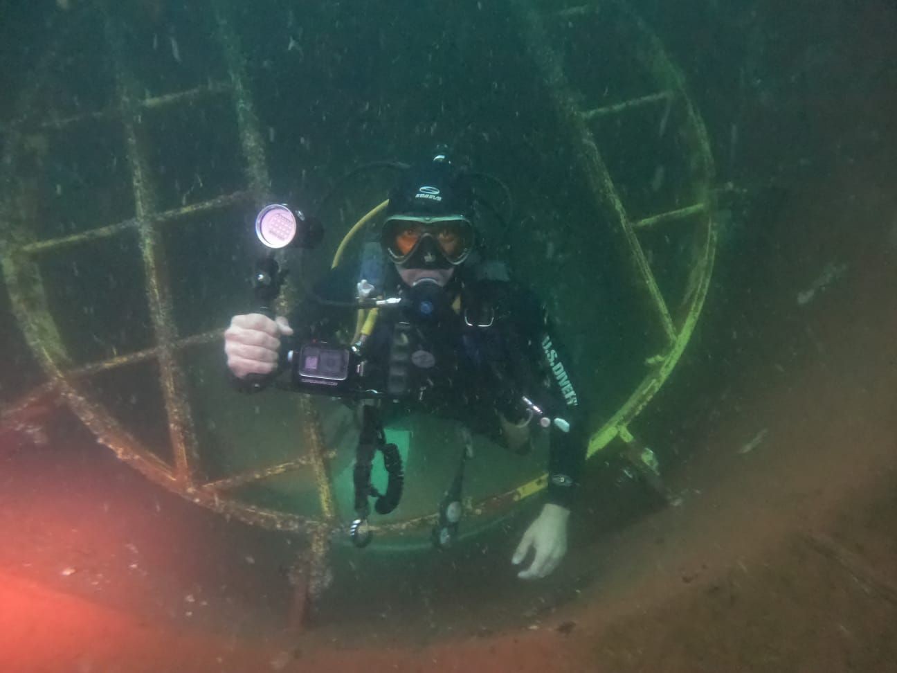 Scuba diver exploring an underwater structure with a flashlight and camera in hand.