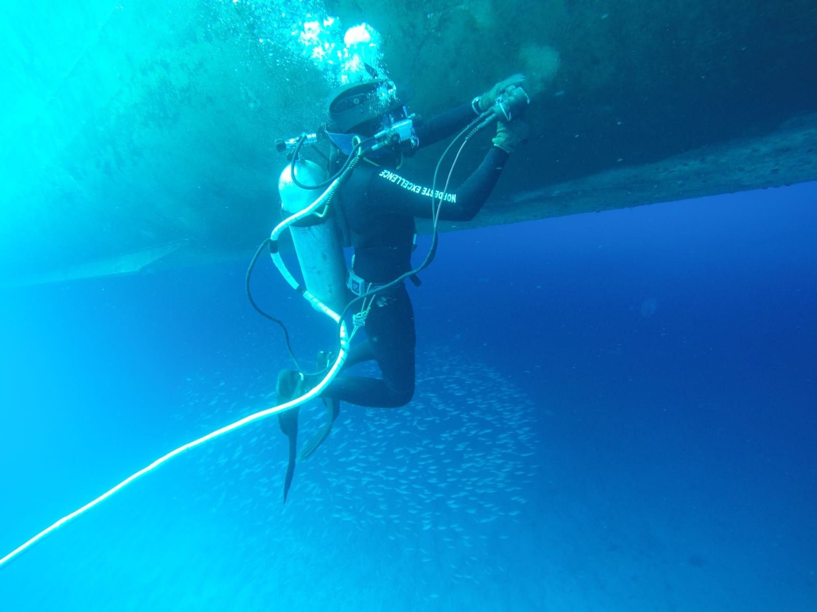 Scuba diver cleaning the underside of a boat in clear blue water.