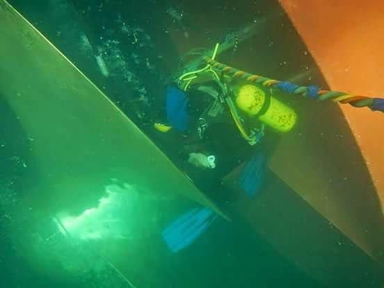 Diver in full scuba gear submerged between large orange and green structures underwater.